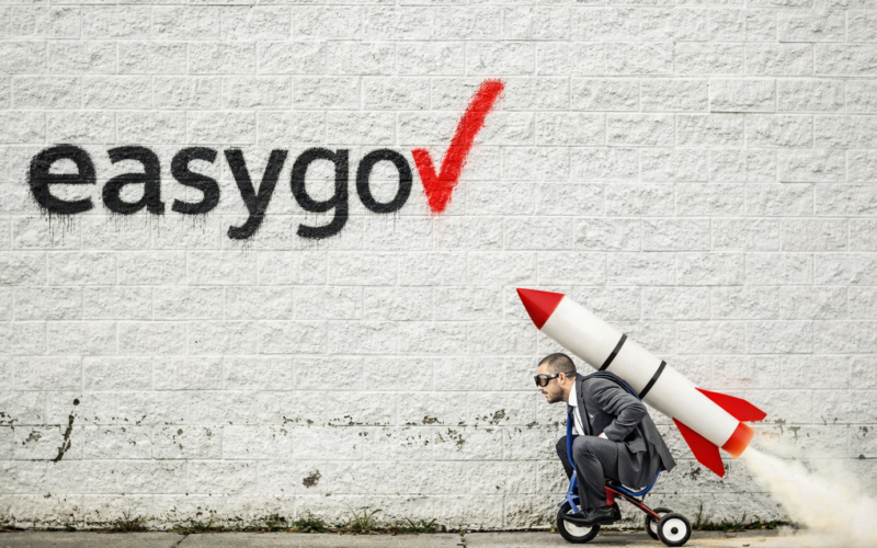 easygov auf eine Mauer gesprayt, davor ein Mann auf einem Dreirad mit einer Rakete auf dem Rücken